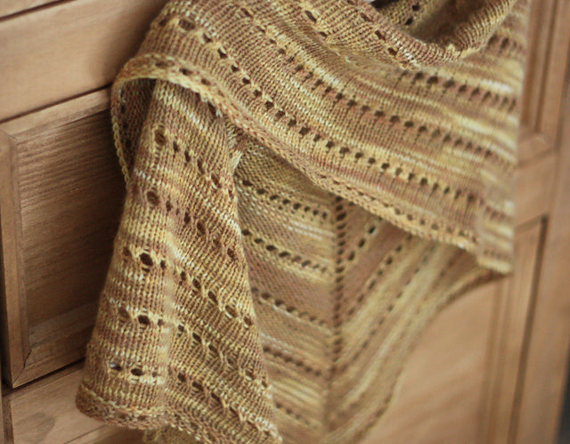 A triangular shawl in shades of yellow and brown with stripes of eyelet lace