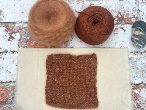 a rust coloured fluffy knitted swatch, which has a bit of a marled appearance to it thanks to the fluffy yarn being slightly lighter than the smooth yarn