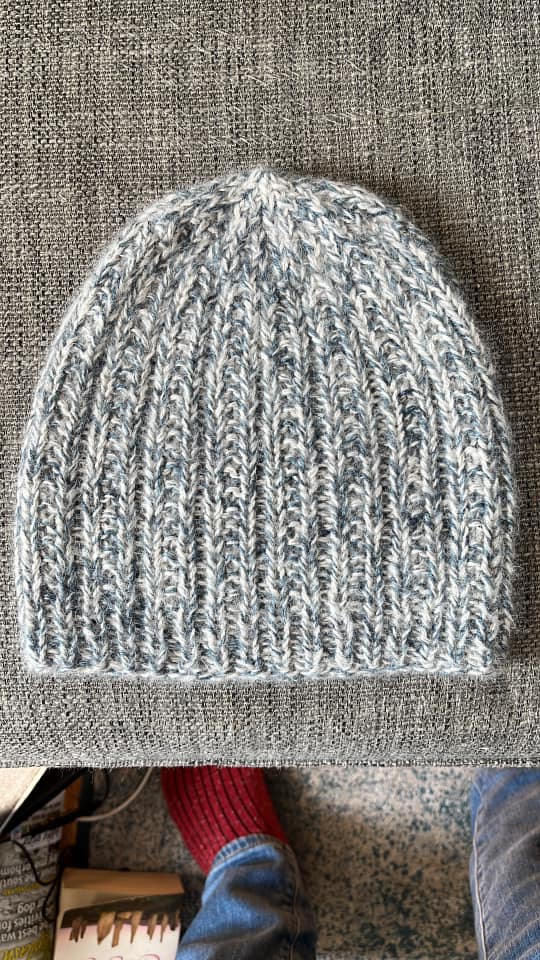 A marled blue and cream knitted hat resting on a grey surface