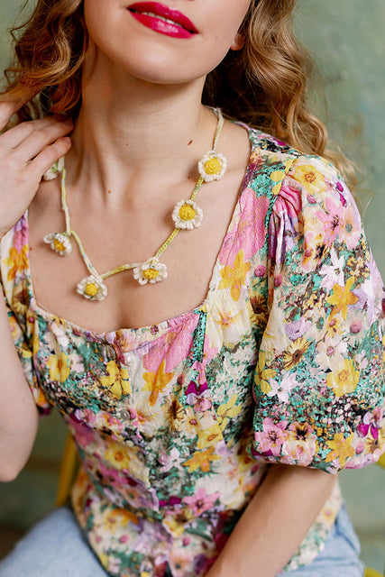 A person wearing a flowery top with a necklace made of crochet daisies and a crochet chain