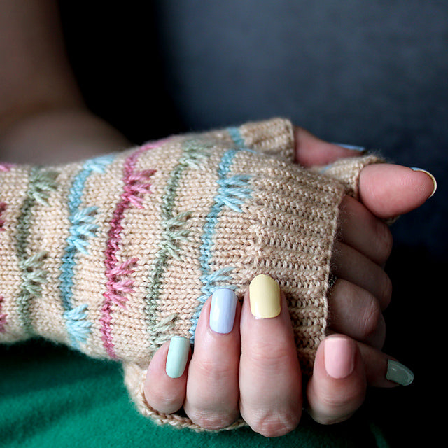 A pair of hands wearing beige fingerless mitts with blue, green and red details