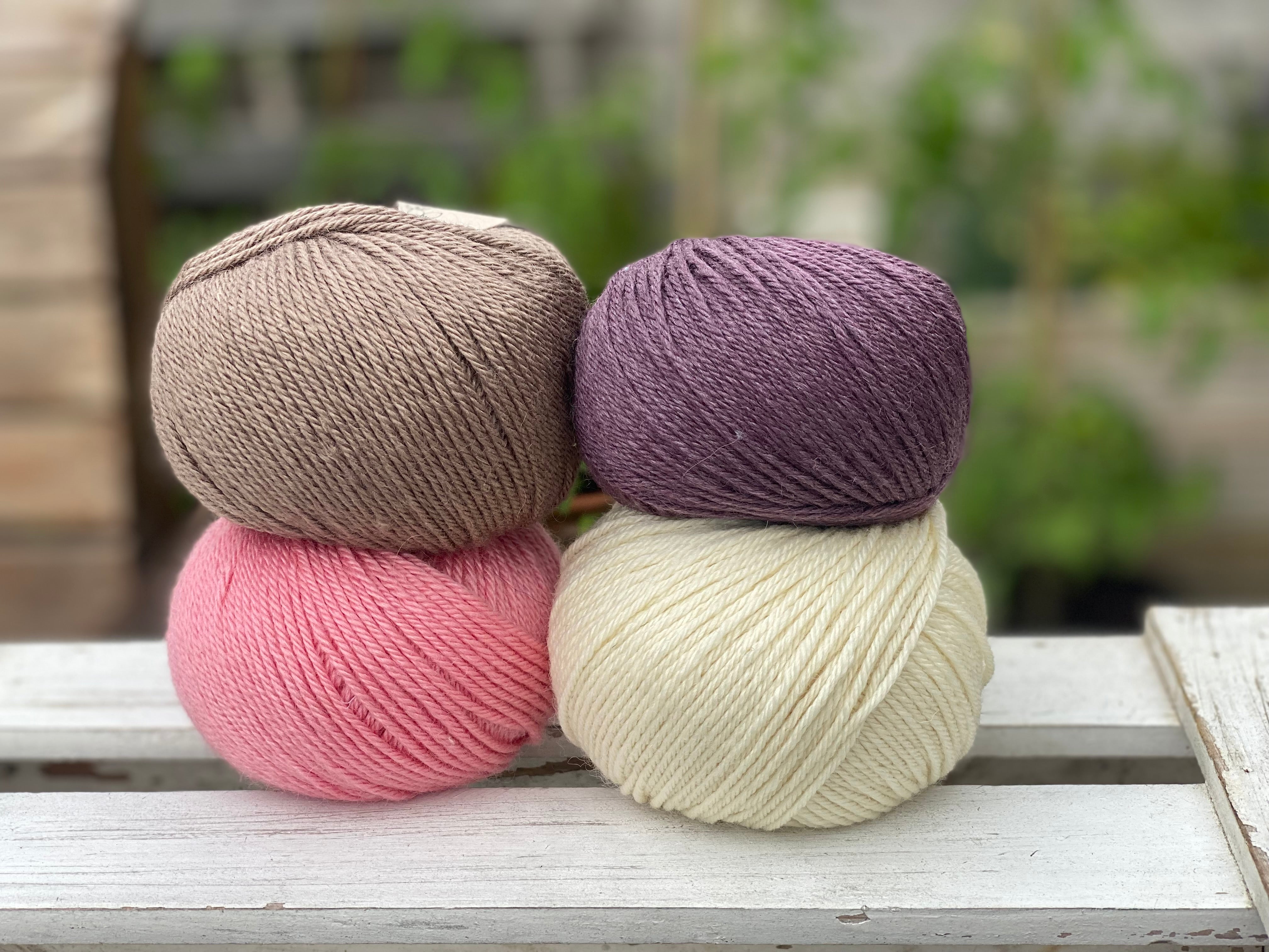 Four balls of yarn in two rows of two. There is a brown ball, a dark purple ball, a pink ball and a cream ball.