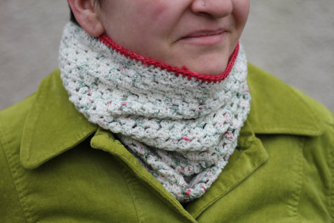 Victoria wearing a crochet cluster cowl in variegated cream, green and red yarn with a red edging. The yarn has silver sparkle running through it
