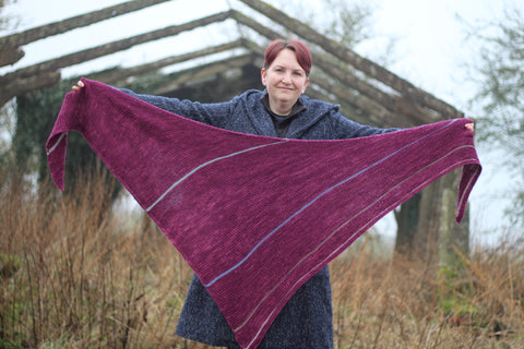 Victoria holding a purpley pink triangular shawl outstretched. The shawl has stripes in muted contrast colours