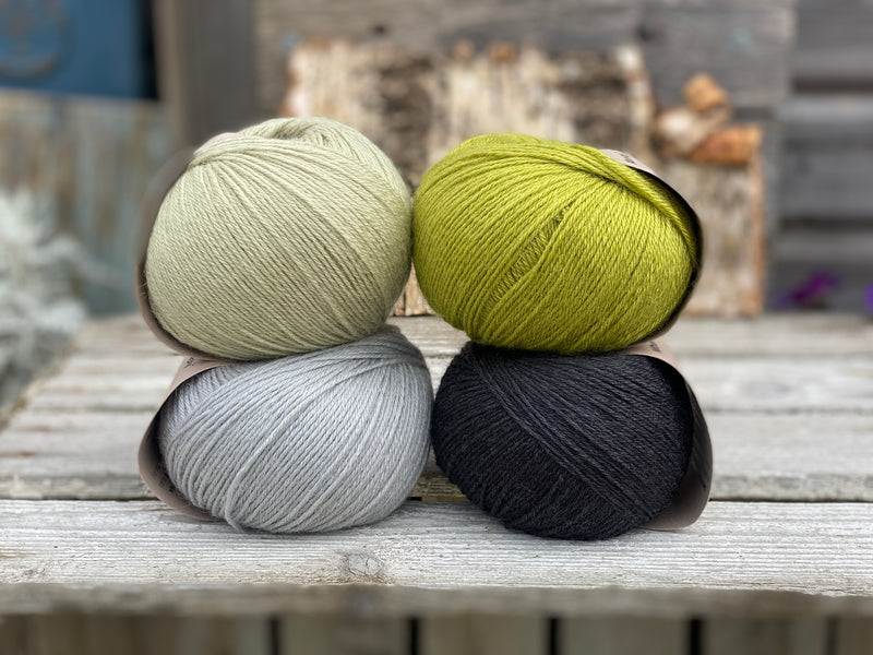 Four balls of yarn arranged as two rows of two balls. The top row is a light green ball and a bright green ball. The bottom row is pale grey and very dark grey