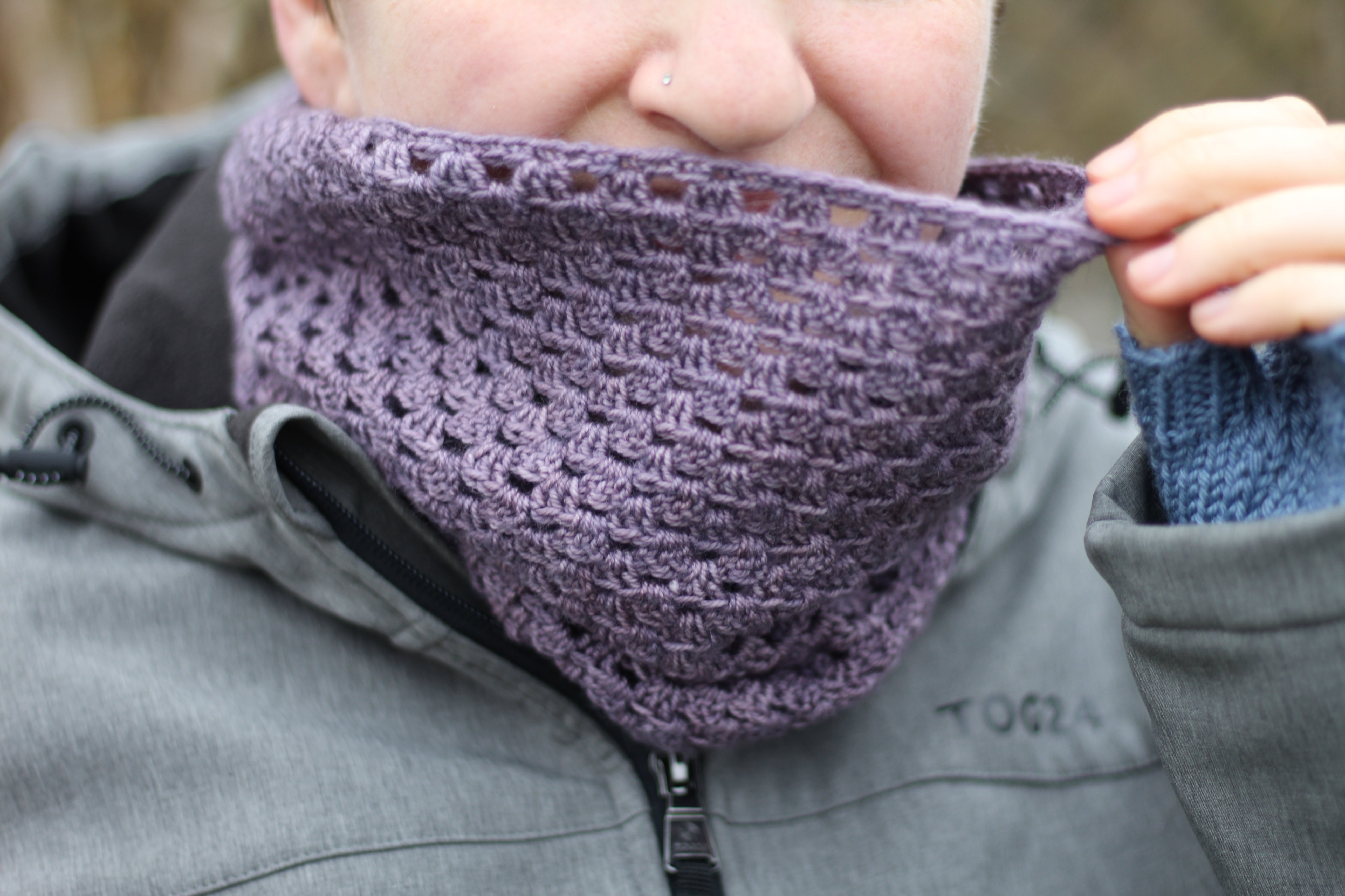 Victoria wearing a purple granny stripe cowl and pulling it up to partially cover her face.