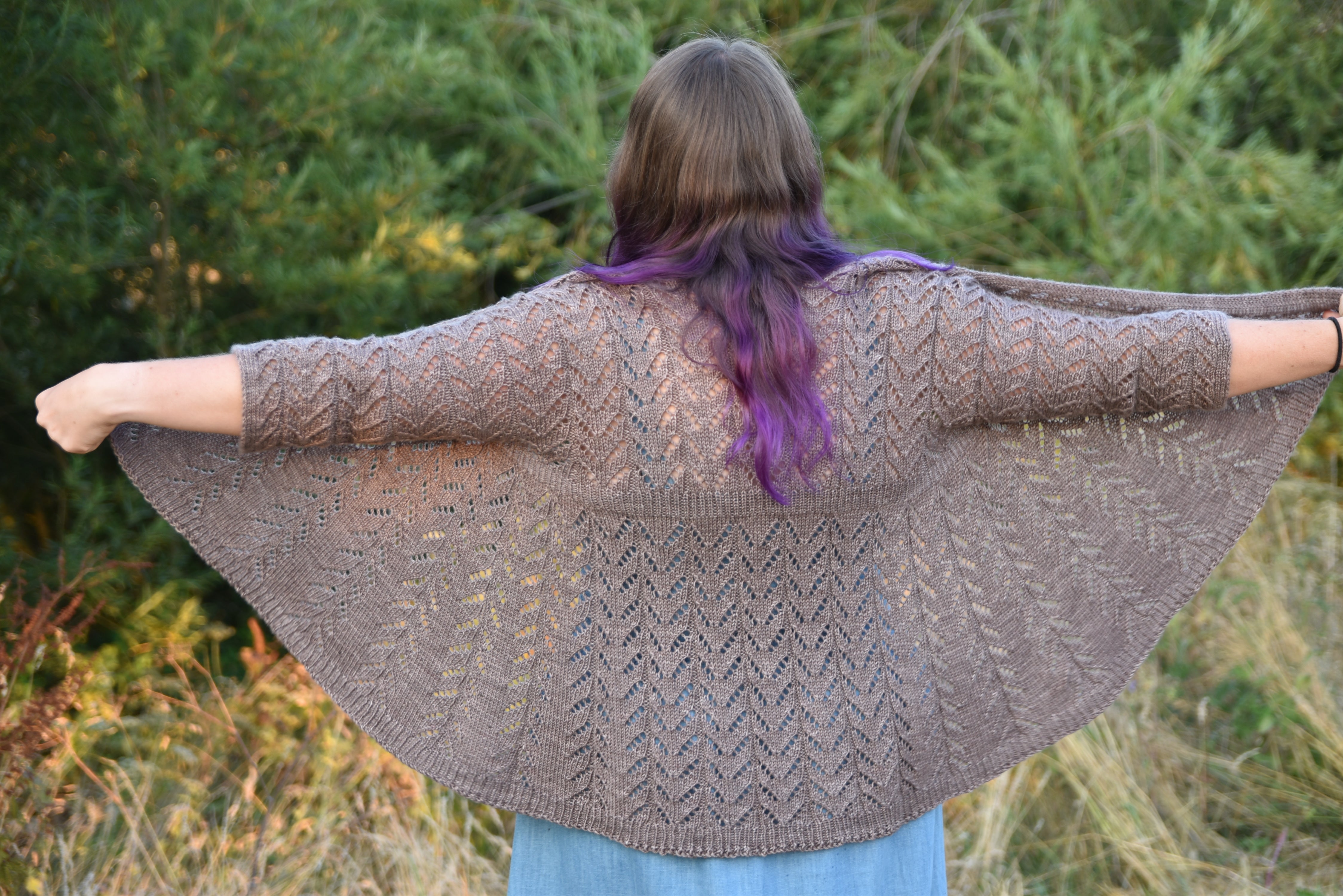 Victoria facing away from the camera wearing a brown lace cardigan. The sides are held out to show the wingspan of the design