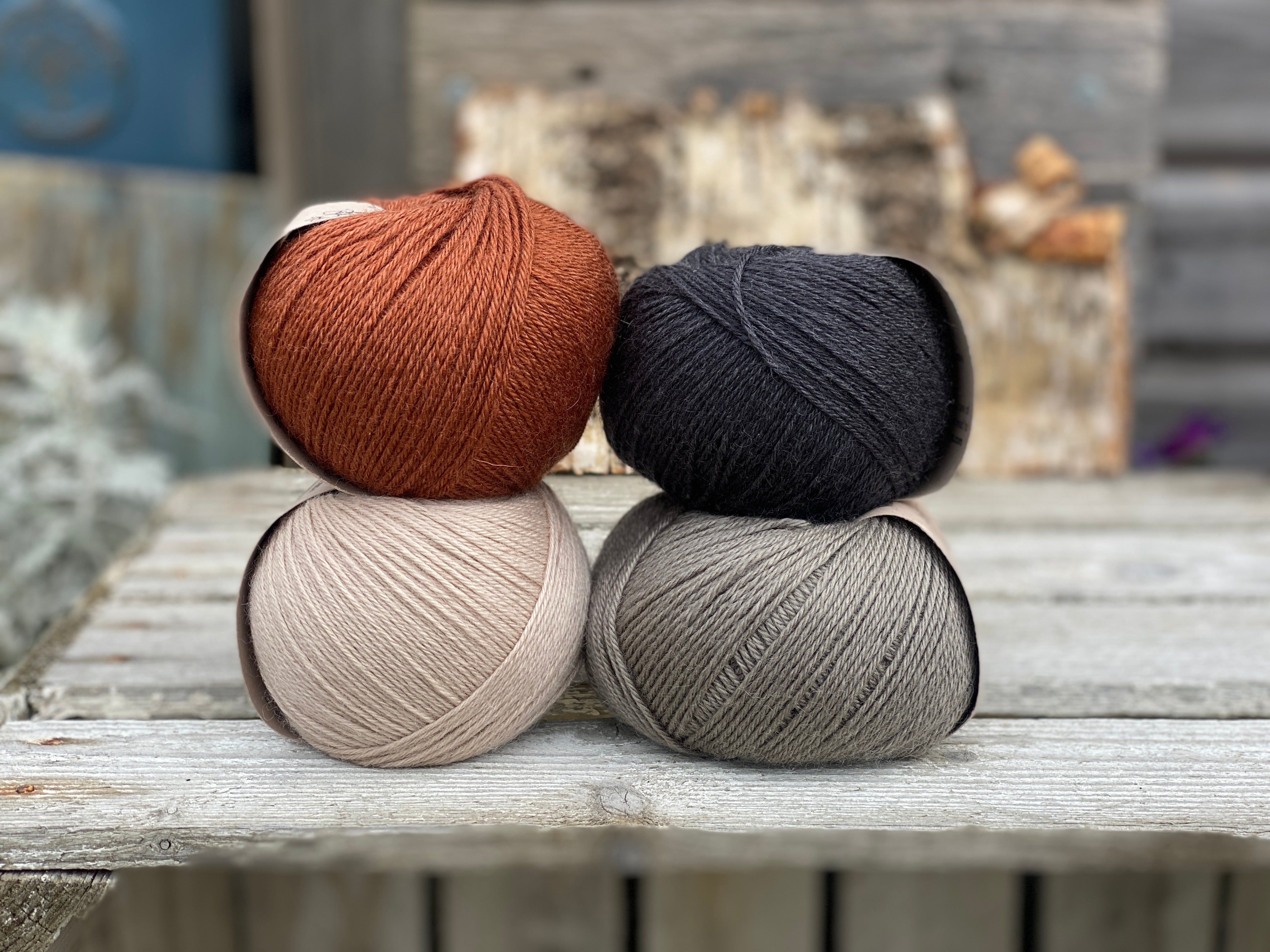 Four balls of yarn. There is a reddish-brown ball, a dark grey ball, a beige ball and a grey ball.