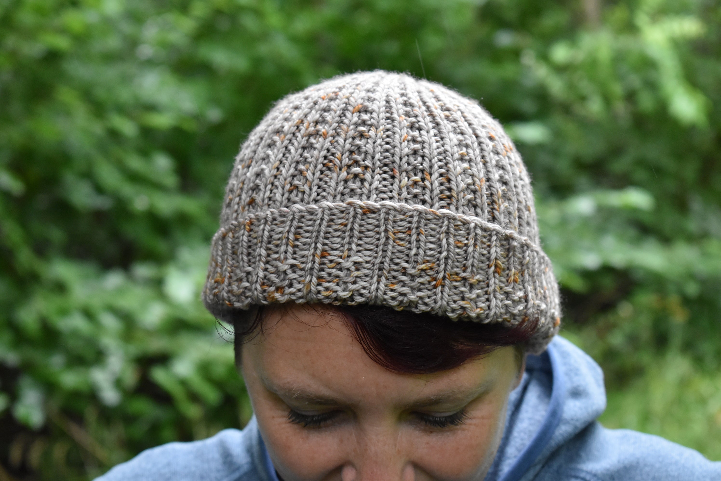 Victoria looking towards the floor wearing a light brown hat with orange speckles. The brim of the hat is upturned