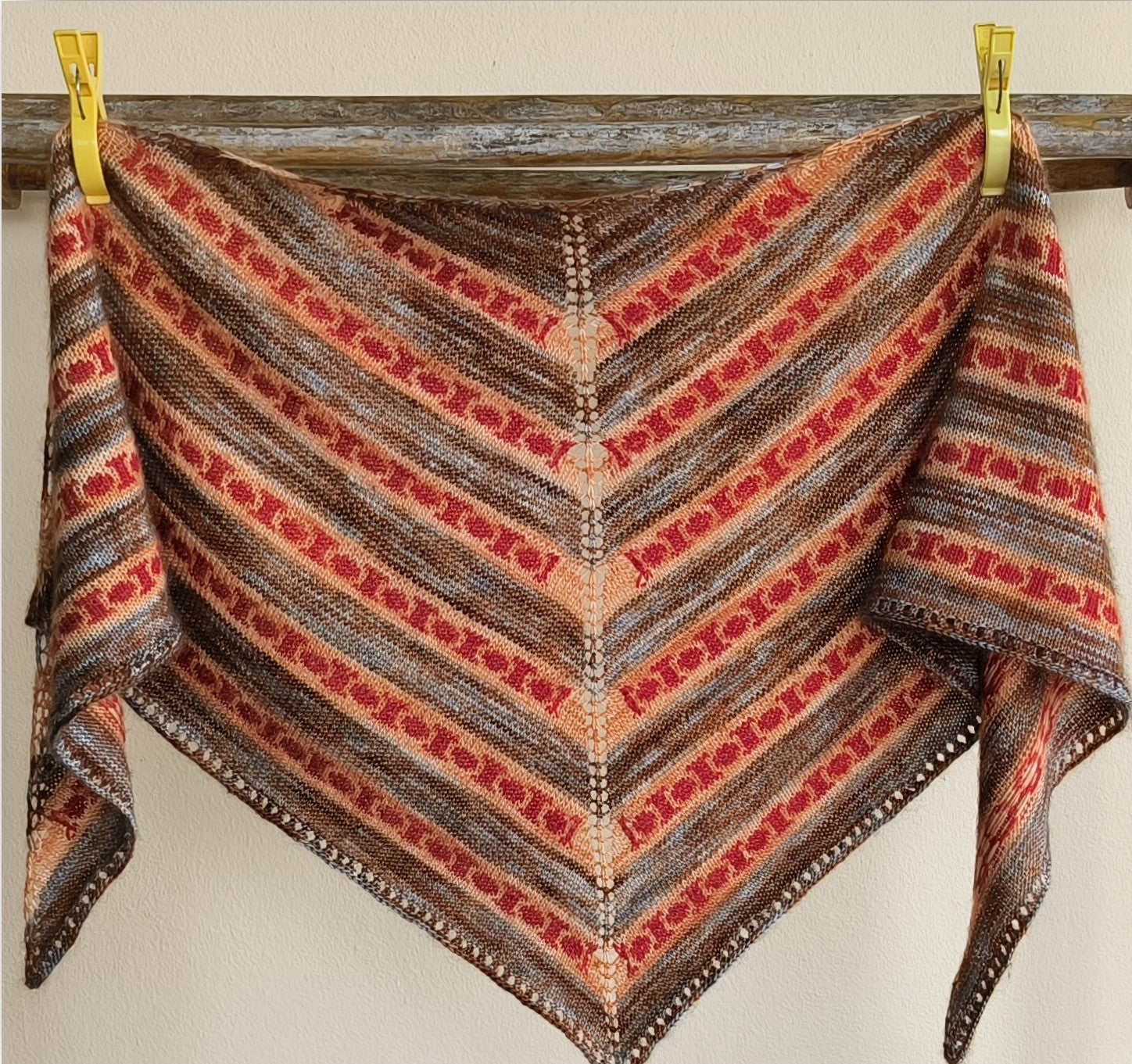 A triangular shawl with alternating stipes of brown with orange and red colourwork