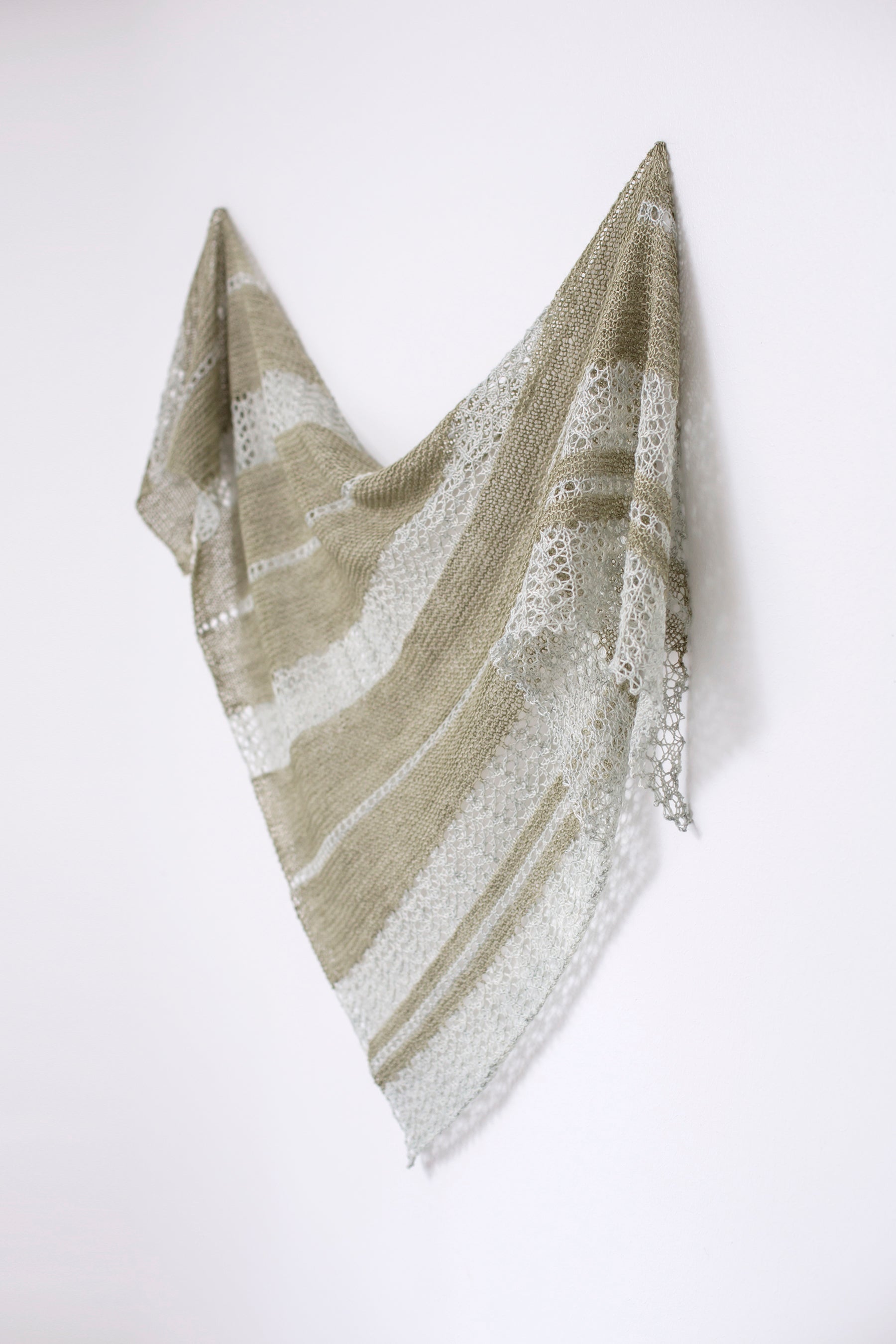 A two colour striped triangular shawl. The green and pale blue-grey stripes are irregularly sized and work from one corner to the opposite edge.