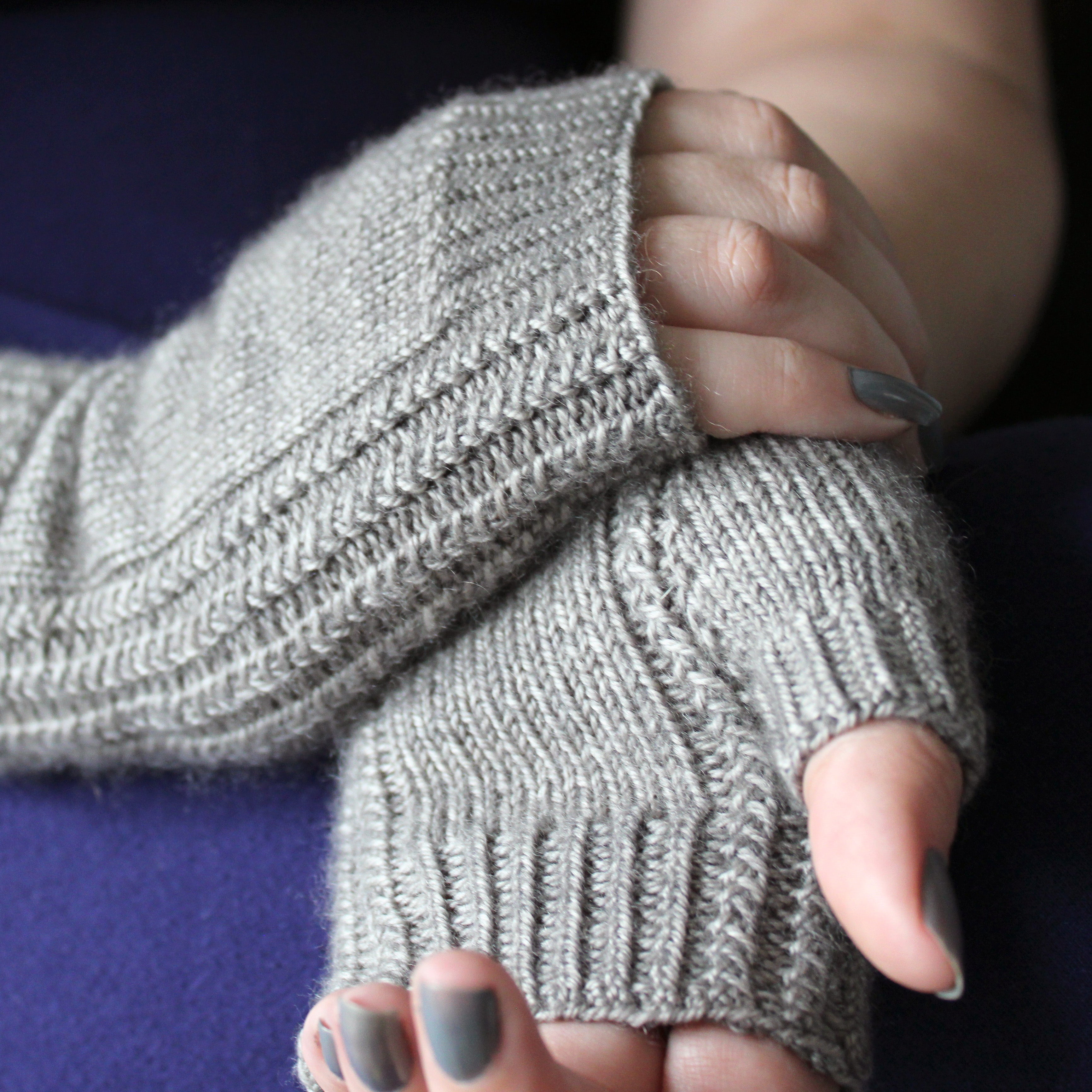 A pair of grey fingerless mitts with a textured stitch pattern running down the side of the hand