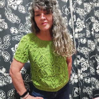 A person wearing a green tee with intricate cable detailing throughout