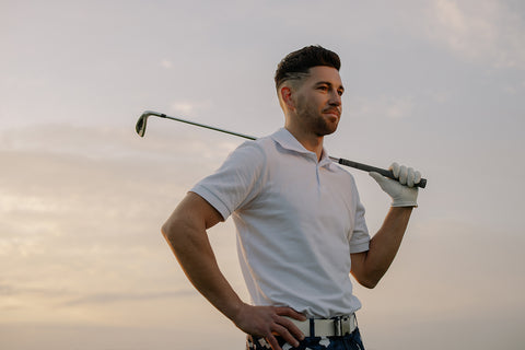 man wearing golf clothes for golfing and holding a golf club over his shoulder while looking and smiling