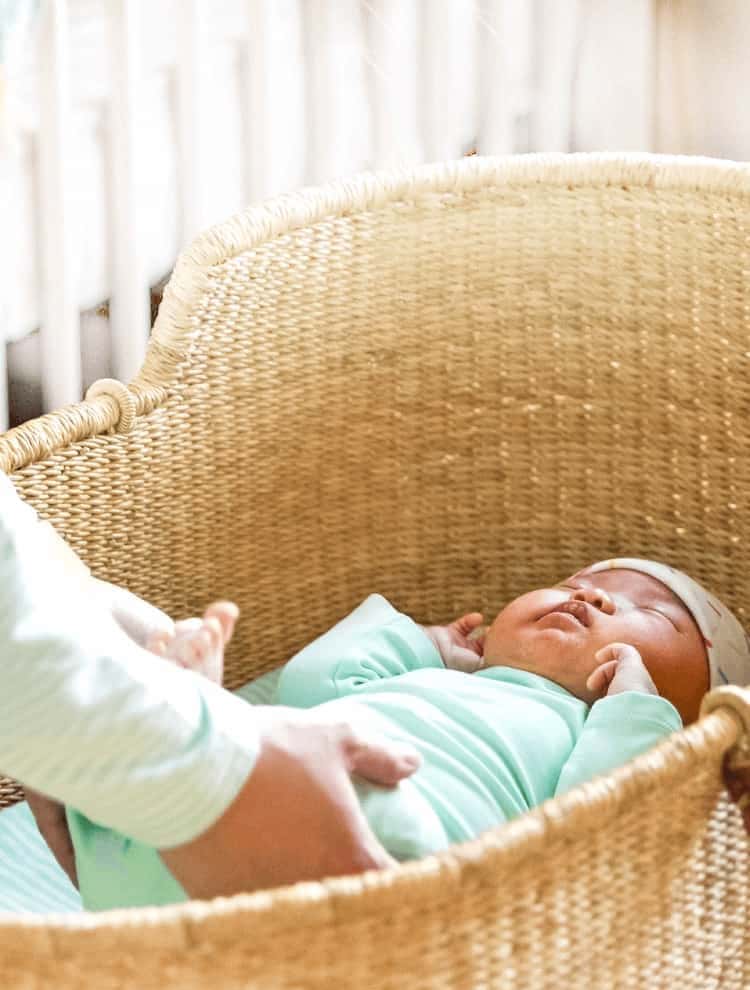 mother reaching for baby in wicker bassinet