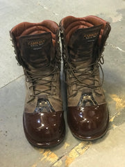 Pair of brown work boots with reinforced glossy toe caps, displayed on a concrete floor.