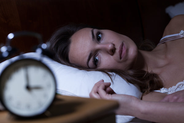 Woman awake at night looking at her nightstand clock because of her insomnia, which causes leaky gut.