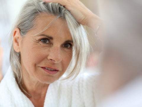 Older woman with short grey hair looking at herself in the mirror