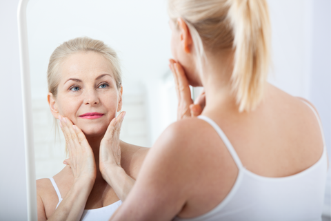 older woman looking in the mirror holding her face