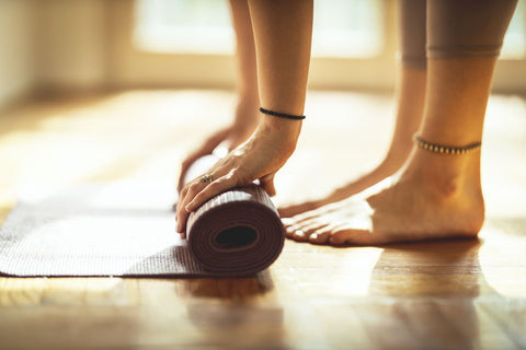 woman rolling up a yoga mat barefoot