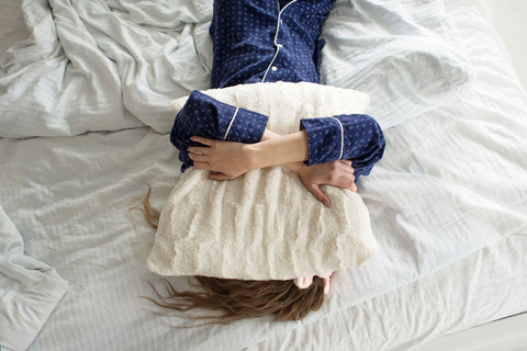 woman holding a pillow over her head laying on bed