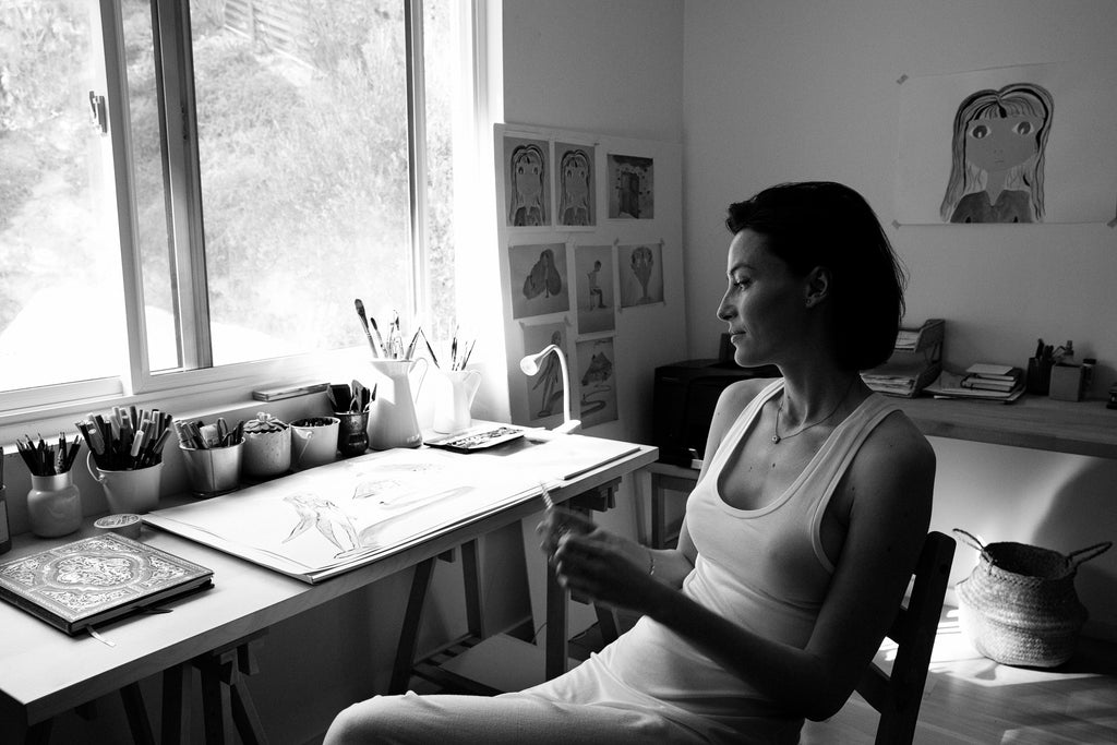 Black & white image of French-born painter, author, and actress Loan Chabanol seated in her studio. 