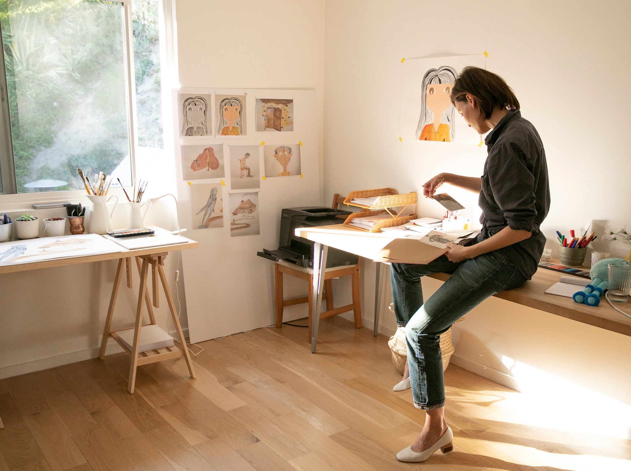 Loan Chabanol seated on one her desks looking through some artwork.