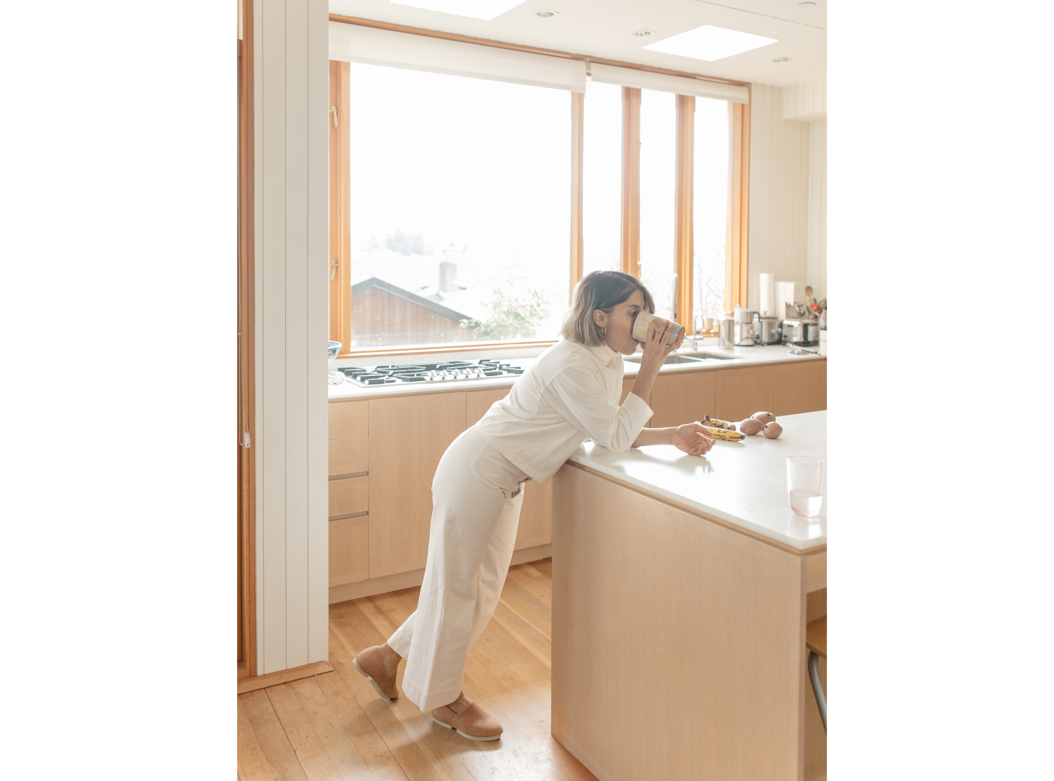 Rubeena Ratcliffe leaning of her kitchen island, drinking. 