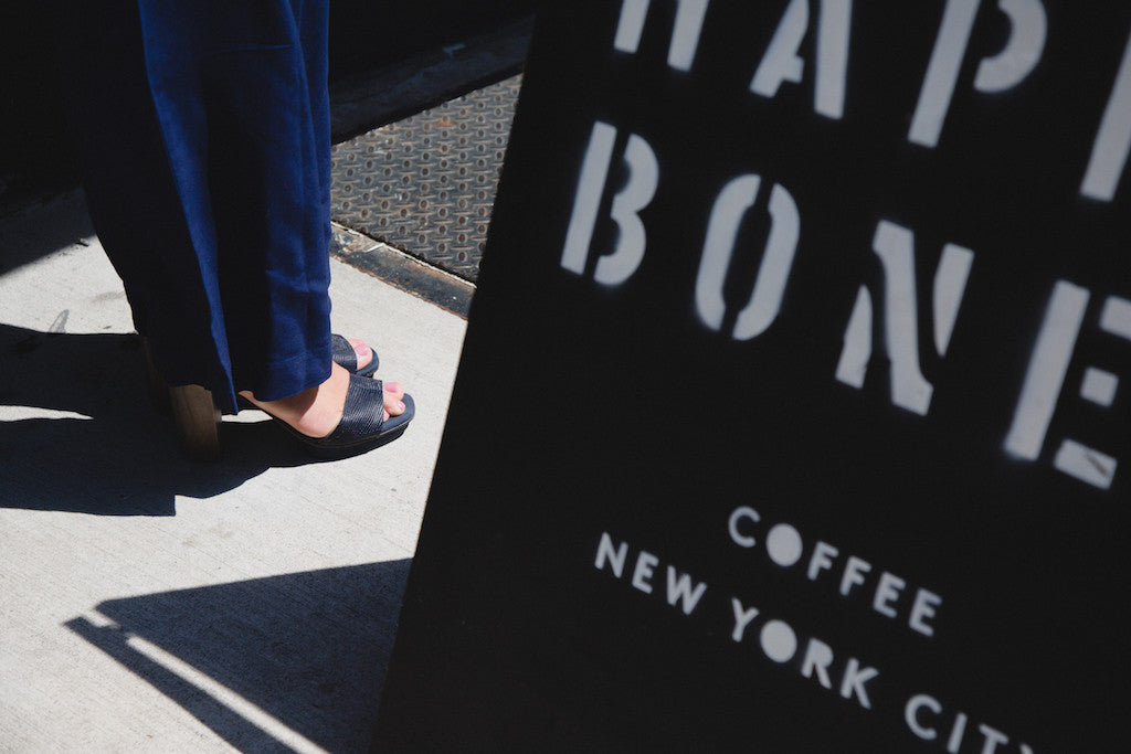 Close up of Amy Woodside modeling the Coclico Leggy Heel beside the Happy Bones nyc street sign. 
