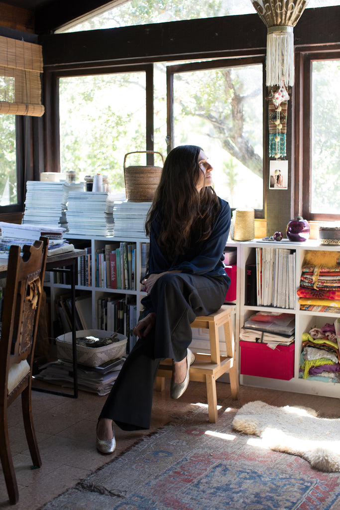 Erica Tanov seated in a sunlit room filled with windows, books and textiles.