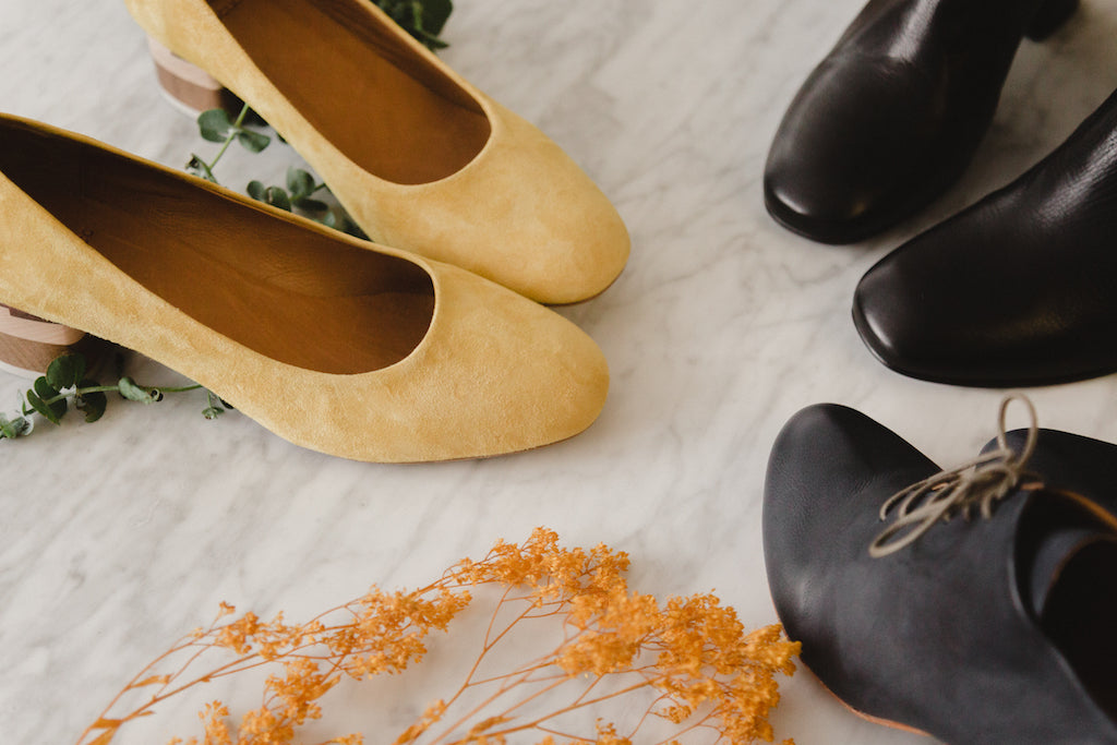 Close up image of three pair of Coclico shoes on a marble counter with decor displayed around shoes. 