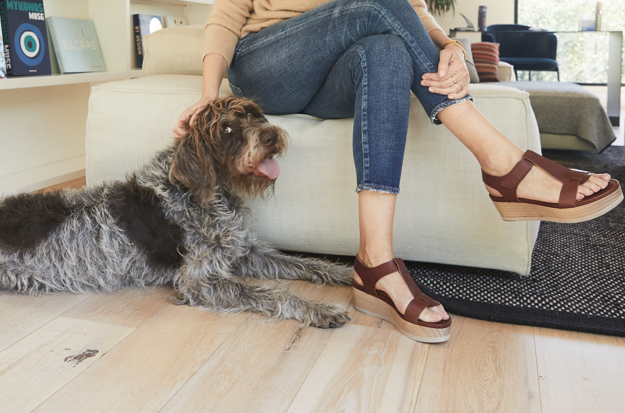 Waist-down image of Mariapaz Fernandez petting her dog while wearing Coclico sandals.