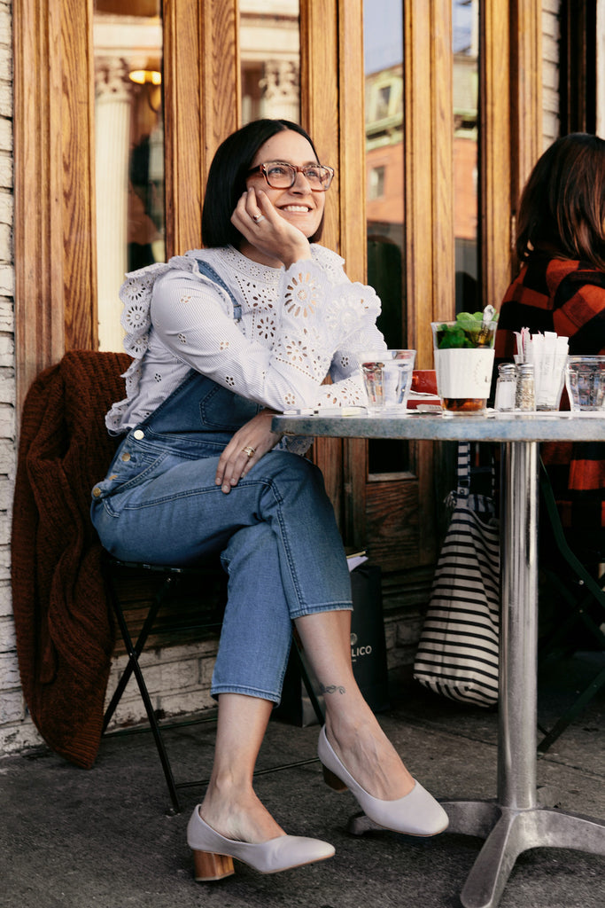 Outdoor image of Maya Jankelowitz from Jack's Wife Freda sitting cross-legged on a table of the bistro. 
