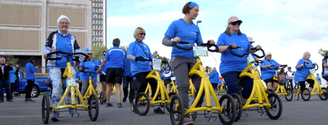 People at their Alinkers at a 2k run event in Ottawa. People on their yellow Alinkers, wearing blue shirts. Participating in an event with 50 Alinker users.