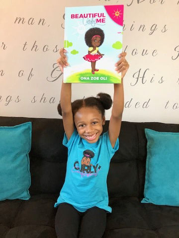 Young girl holding up Beautiful Curly Me book with a huge smile on her face