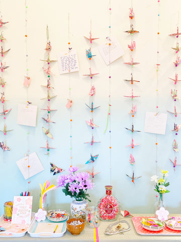 Straight forward view of safe space, including paper crane garlands on wall with note papers attached and offering table