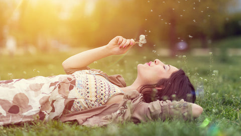 a girl lying in grass blowing dandelions