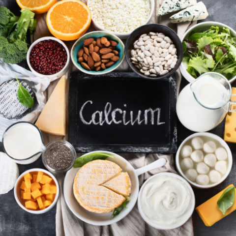 A blackboard with a written text calcium surrounded by different food such as milk, cheese, orange, and other seeds