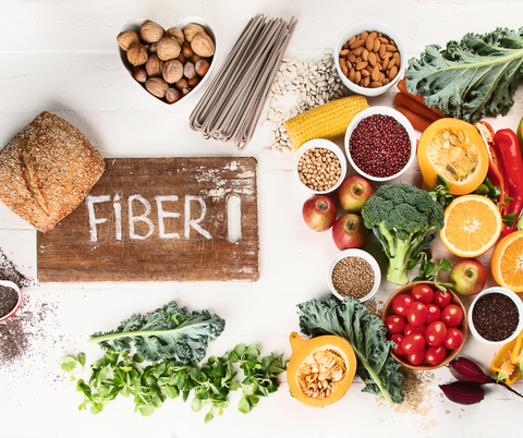 a chopping board with a text "fiber" surrounded by different fruits and vegetables on a table