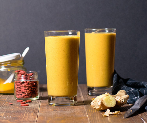 A yellow smoothie in a glass on a wooden table