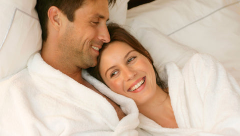 a couple in white robes lying in bed