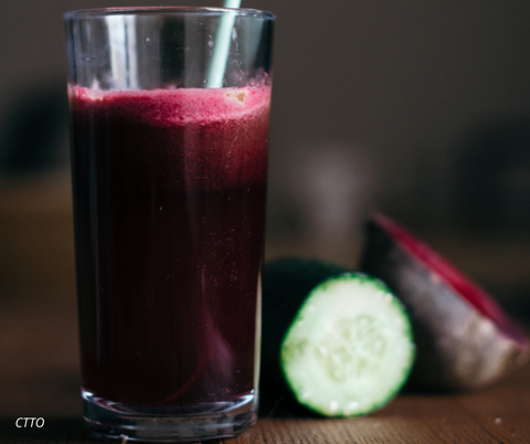 A glass with purple smoothie with deets and cucumber on a wooden table