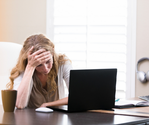 a woman looking at a laptop while holding her head