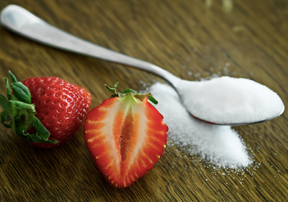 a strawberry cut in half next to a spoon of sugar