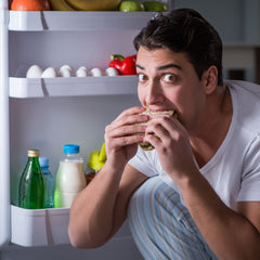 a person eating a sandwich in front of a refrigerator