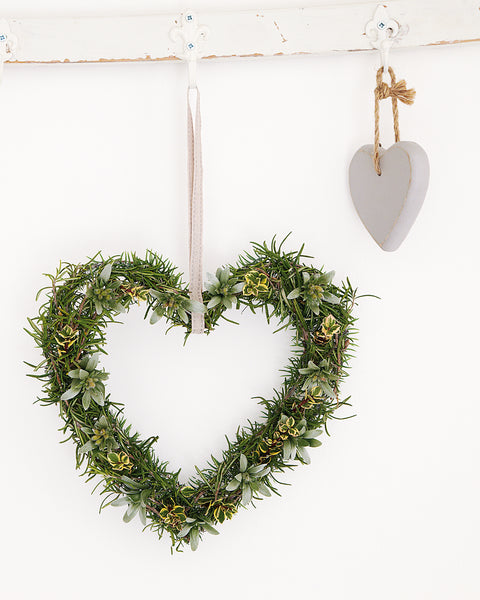 Rosemary heart shaped wreath hanging on a white wall