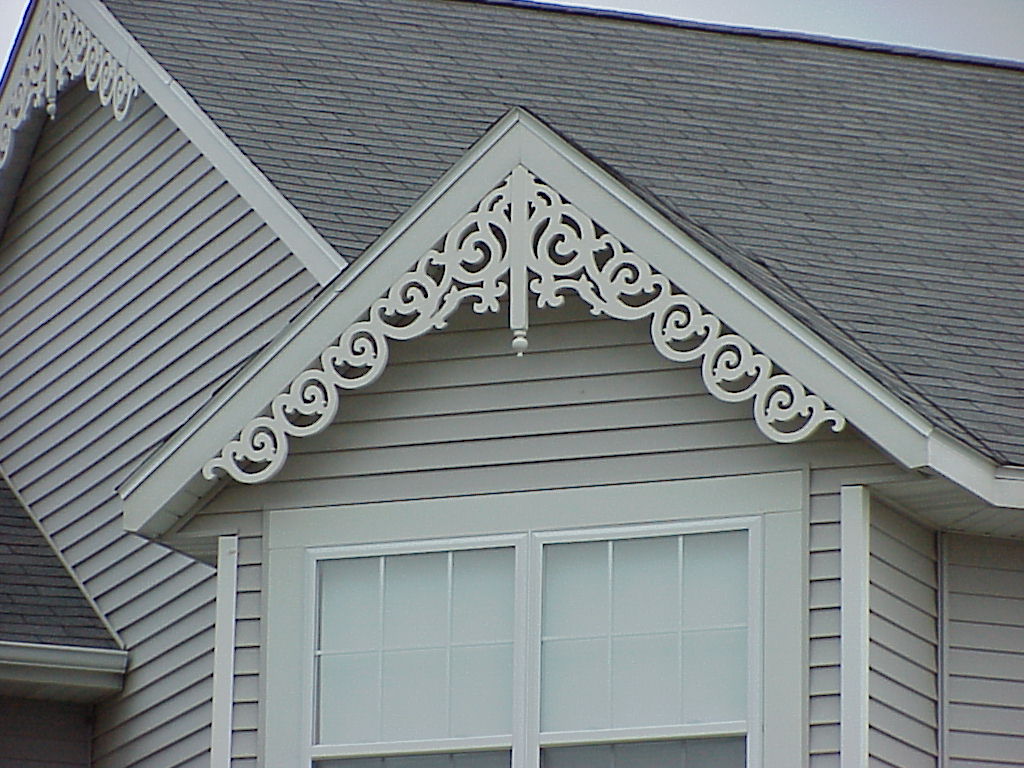 A grey home has a white gingerbread-style gable decoration.