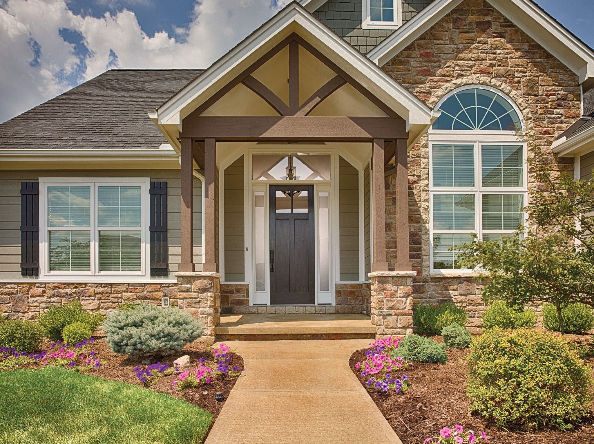 This house has a covered front porch accentuated by a Craftsman -style wood gable decoration and beautiful landscaping on the sides of the walkway and porch.