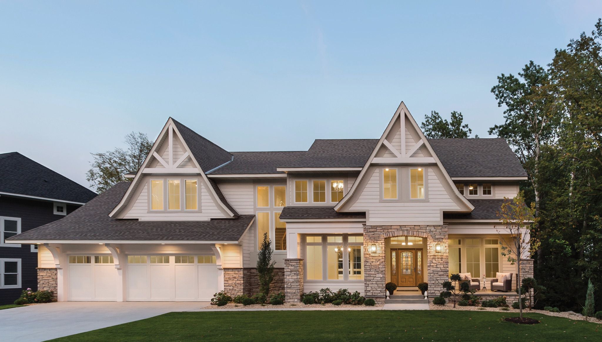 This two-story home has stone and tan siding. There are beautiful decorative gable trusses and long, rectangular windows.