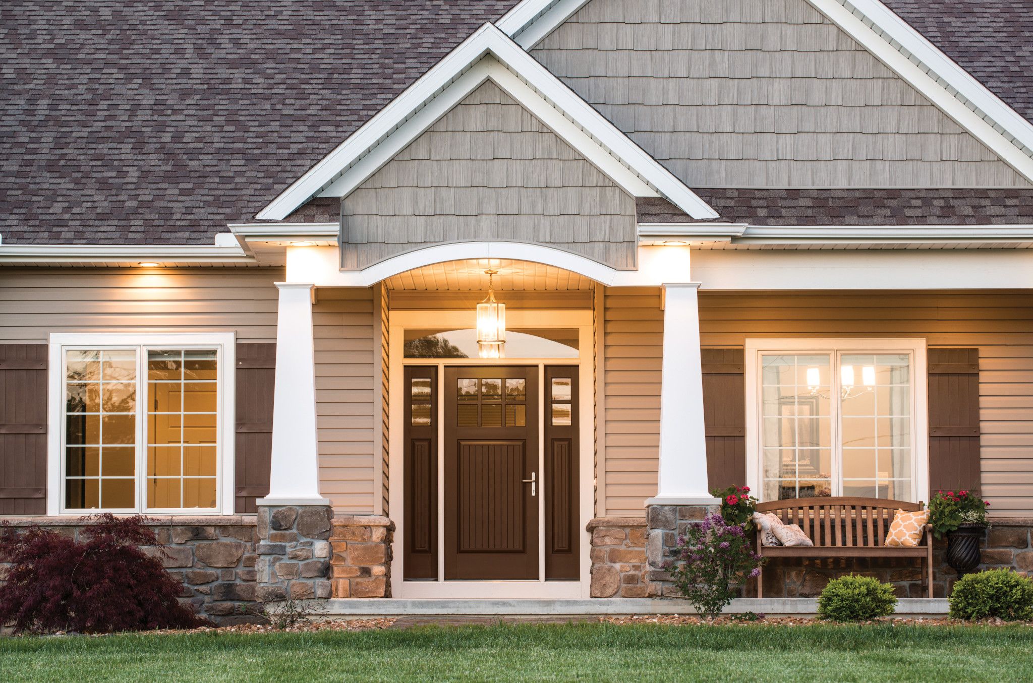 This home has tan and stone siding with brown shudders. There is a hanging light fixture in front of the brown door.